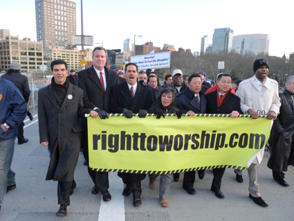 Pastors and officials including Public Advocate Bill de Blasio (holding banner second from left) and Comptroller John Liu (holding banner second from right) joined thousands of churchgoers Sunday afternoon in a march across the Brooklyn Bridge to protest the cityâ€™s plan to ban churches from renting space in public schools.	Eagle photo by Mary Frost