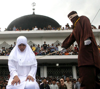 A Shariah law officer canes a woman at a mosque in Indonesia, after the woman was caught staying with her boyfriend in a house. 	AP Photo/Binsar Bakkara