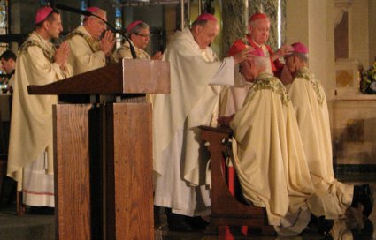 Archbishop Emeritus of New York Edward Cardinal Egan (wearing magenta robes) lays hands on the Most Rev. Paul R. Sanchez, D.D., as Archbishop Philip Wilson of Adelaide, Australia (in white robes), lays hands on the Most Rev. Raymond F. Chappetto, D.D., during the ordination liturgy Our Lady of Angels Church in Bay Ridge. At left are Principal Co-Consecrating Bishops the Most Reverends Frank J. Caggiano, Nicholas DiMarzio and Octavio Cisneros. Bishop DiMarzio heads the Diocese of Brooklyn; Bishops Caggiano and Cisneros are the other two Auxiliary Bishops. All the Bishops present took turns laying their hands on the new prelates. Eagle photo by Francesca Norsen Tate.