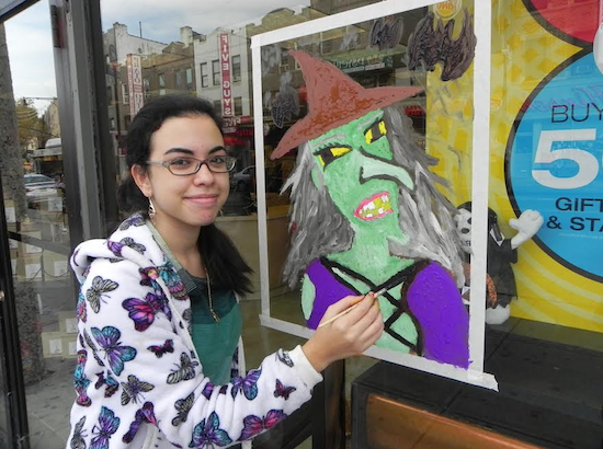 Fort Hamilton High School student Nardine Karam puts the finishing touches on her painting of a wicked witch on the window of American Greetings, a gift shop on Fifth Avenue.