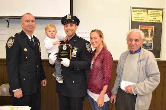 At this month's 84th precinct community council meeting, Captain Sergio Centa (left) and council president Leslie Lewis (right) honored officer Joseph Swicicki (center with one-year-old son Hunter and wife Corinne) for removing an illegal handgun from the streets. Eagle photo by Rob Abruzzese