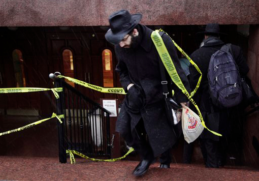 A member of the Lubavitch community walks through crime-scene tape as he leaves Chabad-Lubavitch Hasidic headquarters on Tuesday in New York. Earlier, a knife-wielding man stabbed an Israeli student inside the Brooklyn synagogue before being fatally shot by police after he refused to drop the knife. The student, Levi Rosenblatt, is in stable condition. AP Photo/Mark Lennihan