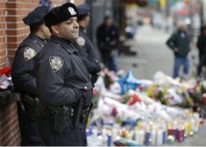 New York City police officers watch over a makeshift memorial near the site where fellow officers Rafael Ramos and Wenjian Liu were murdered in Brooklyn. Police say Ismaaiyl Brinsley ambushed the two officers in their patrol car in broad daylight Saturday, fatally shooting them before killing himself inside a subway station. AP Photo/Seth Wenig