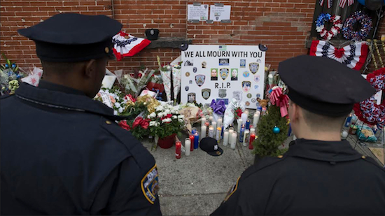 NYPD officers visit a makeshift memorial near the site where fellow officers Rafael Ramos and Wenjian Liu were murdered in Brooklyn on Monday. AG Eric Holder is directing the Justice Department to expedite death benefits to the families of two New York police officers who were fatally shot inside their patrol car. AP Photo/John Minchillo
