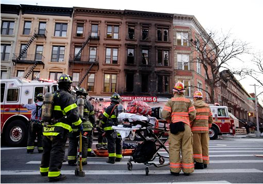 Firefighters and paramedics stand at the scene of a 5-alarm fire where one person died and eight other people were injured in Brooklyn on Wednesday. About 30 people have been displaced by the fire. AP Photos/Peter Morgan
