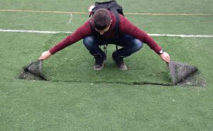 A student demonstrates how easy it is to pull the athletic field’s turf up like a rug. Photo courtesy Nick Koven