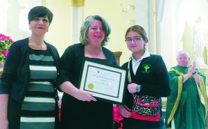 Saint Patrick Catholic Academy Principal Andrea D’Emic (left) and eighth-grader Helen El-Achkar (right) present the Distinguished Graduate Award to Hon. Vera Scanlon, magistrate judge for the U.S. District Court in the Eastern District of New York, as the Rev. Msgr. Michael Hardiman applauds.