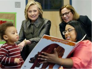Hillary Rodham Clinton, left rear, and Laura Ensler listen as an instructor reads a story to children at an FirstStep NYC, an early childhood development center in the Brooklyn borough of New York, Wednesday, April 1, 2015.Clinton is teaming up with New York's first lady and deputy mayor in introducing a program to encourage parents to talk and read to their young children, no matter how young. AP Photo/Kathy Willens, Pool