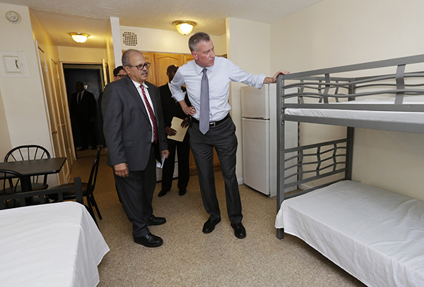 New York Mayor Bill de Blasio, right, listens to Acacia Network CEO Raul Russ, as he visits a room at the Corona Family Residence, a homeless facility in Queens. AP Photo/Richard Drew, Pool