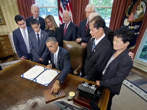 President Barack Obama reaches for a pen as he signs S. 665, the Rafael Ramos and Wenjian Liu National Blue Alert Act of 2015 on Tuesday in the Oval Office of the White House in Washington. From left are, Justin Ramos, 19, Jayden Ramos, 14, Vice President Joe Biden, Maritza Ramos, Sen. Ben Cardin, D-Md., Rep. Dave Reichert, R-Wash., Rep. Bill Pascrell, D-N.J., Wei Tang Liu, and Xiu Li. AP Photo/Pablo Martinez Monsivais