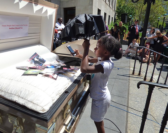 During the press conference, Leilani Charlery, 8, took pictures of the photographs of the gun victims lining the coffin at Borough Hall.  Photo by Mary Frost