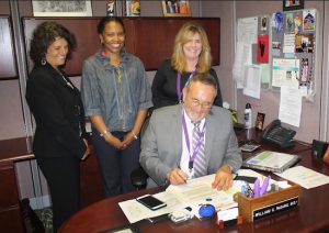 Dr. William Pagano, medical director of the NYU Lutheran Family Health Centers, signs the colon cancer prevention pledge as Christina Farber (left), senior director of primary care systems at American Cancer Society; LaToya Williams (center)  account representative of primary care systems at American Cancer Society; and Judy McLaughlin, RN, vice president of operations at NYU Lutheran Family Health Centers, look on. Photo courtesy of NYU Lutheran.