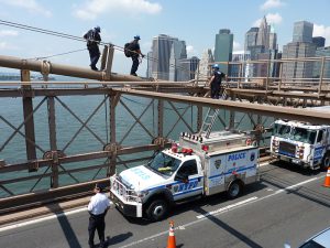Police swarm the Brooklyn Bridge after German artists replaced the American flags atop the towers of the bridge in 2014. Photo by Mary Frost