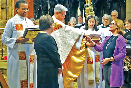 The Rev. Stephen D. Muncie hands the keys to Grace Church to the parish’s Junior Warden, Kate Rock (wearing purple) as Senior Warden Vivian Toan (foreground) and members of the Parish Choir watch. At left, holding the Gospel book, is the Rev. Nan Peete, a longtime friend of Muncie’s. Photo credit: Martin Friedman