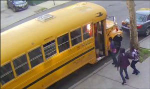 In this frame grab taken from surveillance video, children watch as pieces of cardboard they placed on a school bus begin to burn on Sunday, May 8, in Crown Heights. Beth Rifkah School via AP
