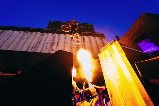 A stunt biker goes off a jump in front of the abandoned Red Hook Grain Terminal while a fire breather performs below. Photo by Khadija Bhuiyan