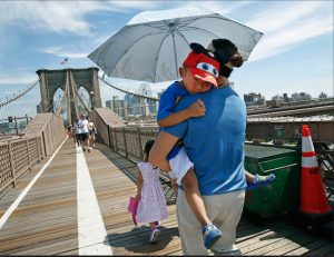 A woman carries her grandson beneath an umbrella as she walks across the Brooklyn Bridge. Transportation officials in New York City say they're exploring options to expand the Brooklyn Bridge's walkway to accommodate pedestrian and bicycle traffic. AP Photo/Kathy Willens