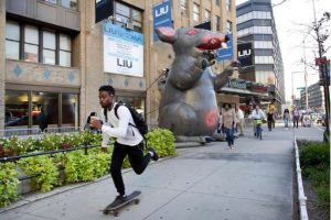 A student skateboards to class at Long Island University's Brooklyn campus, Tuesday, Sept. 13, 2016 in New York. Behind him is an inflatable rat, part of a demonstration by the school's faculty. An agreement to end the lockout was reached on Thursday. AP Photo/Mark Lennihan