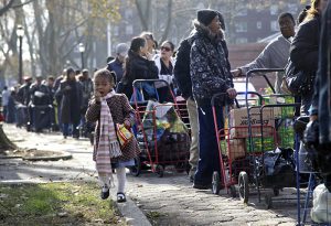 In this November 2012 photo, taken two weeks after Superstorm Sandy, Amber Whichard, 3, walks next to a line of people waiting to receive supplies donated to storm victims at the Red Hook Houses, where some of the buildings in the complex were still without power and heat.  AP Photo/Seth Wenig, File