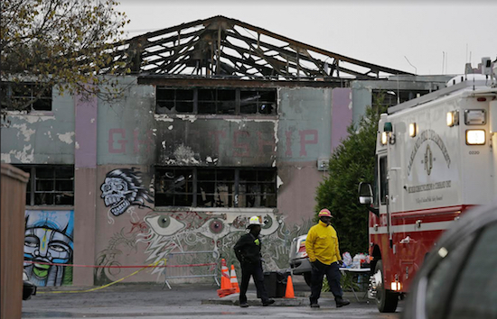 This photo taken on Dec. 7 shows Oakland fire officials walk past the remains of the Ghost Ship warehouse damaged by a deadly fire. The Dec. 2 blaze killed dozens of people during an electronic dance party, according to officials, who said the fire quickly raced through the building and trapped revelers inside. AP Photo/Eric Risberg, File