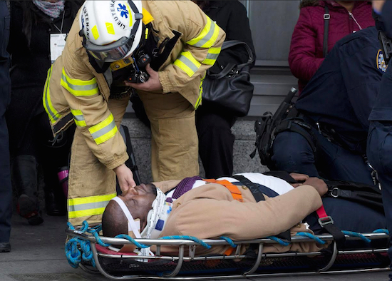 An injured passenger is assisted by an EMS worker as he lies on a gurney outside Atlantic Terminal after a Long Island Rail Road incident on Wednesday. Officials say the investigation into the crash could take days. AP Photo/Mark Lennihan