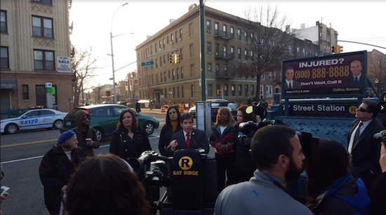 Councilmember Vincent Gentile, pictured at the podium at a 2015 rally calling for better R train service, has endorsed a proposal for low income New Yorkers to get half-fare Metrocards. Photo courtesy of Gentile’s office