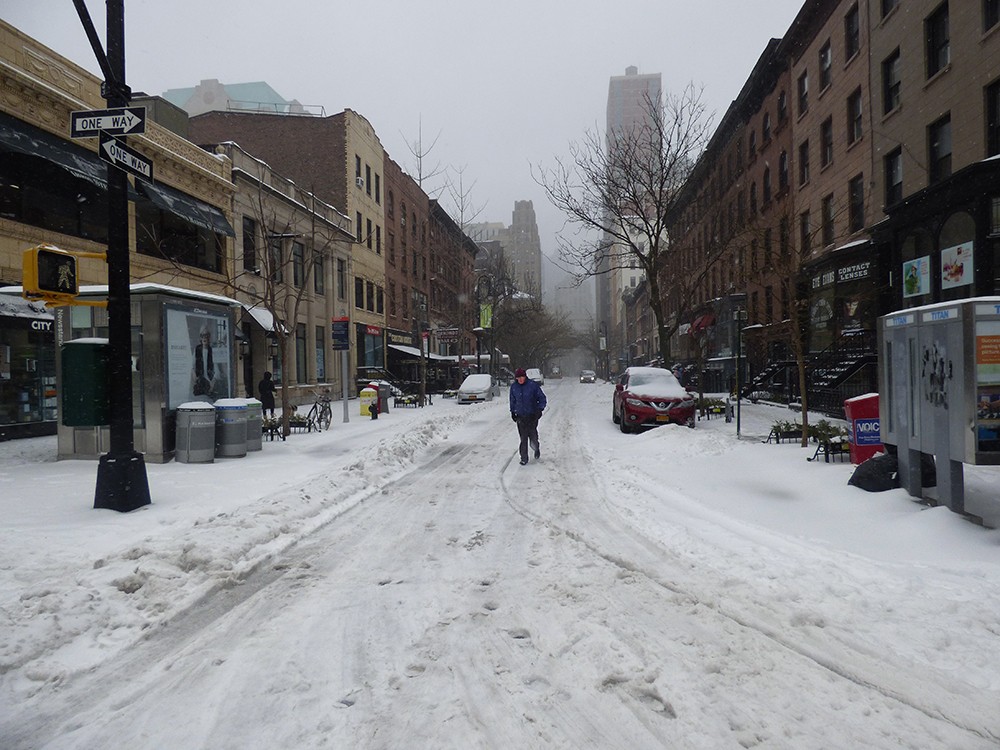 With sidewalks covered by snow, this man takes the easy path down the middle of Montague Street.