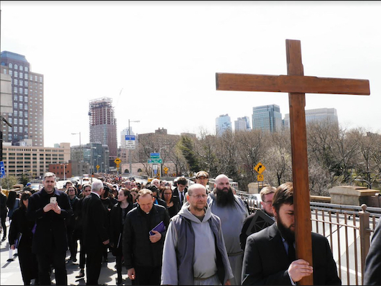 Communion & Liberation sponsors the annual Good Friday Procession across the Brooklyn Bridge. This year, the weather cooperated. Incorporated into the Procession are Stations of the Cross, for which worshipers pause during various points across the bridge. Pictured in front are crucifer Vitaliy Kuzmin, and Franciscan Friars of the Renewal: Brother Giles Barrie, CFR and Fr. Michael Kmiotek, CFR. Eagle Photo by Arthur DeGaeta