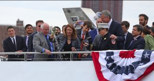 Deputy Mayor Alicia Glen (center with bottle) christens the ferry vessel Lunchbox as Hornblower CEO Terry McCrae (to Glen’s left), Mayor Bill de Blasio, FDNY Chaplain Ann Klansfield (with mic), NYC Environmental Development Corp. President James Patchett (behind Glen) and City Councilmember Vincent Gentile (far right) observe. Eagle photos by Andy Katz