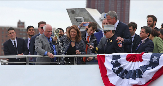 Deputy Mayor Alicia Glen (center with bottle) christens the ferry vessel Lunchbox as Hornblower CEO Terry McCrae (to Glen’s left), Mayor Bill de Blasio, FDNY Chaplain Ann Klansfield (with mic), NYC Environmental Development Corp. President James Patchett (behind Glen) and City Councilmember Vincent Gentile (far right) observe. Eagle photos by Andy Katz