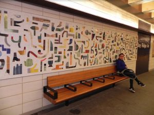 A rider sitting on a bench glances at a new mosaic decorating the wall in the newly renovated Bay Ridge Avenue subway station. The MTA installed several other features to make the wait for an R train more comfortable for riders. Eagle photo by Paula Katinas