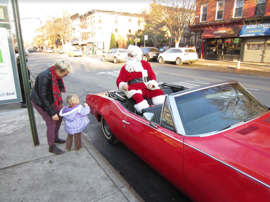 A young girl is thrilled to meet Santa Claus, as he comes around in his vintage Oldsmobile. Photo courtesy of Park Slope Fifth Avenue BID