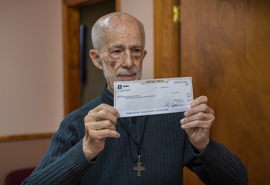Father Ruskin Piedra holds up an $11,000 restitution check from the Brooklyn DA after two of his former employees were caught embezzling funds and cheating clients. Eagle photo by Paul Frangipane