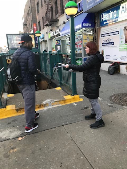 A parent volunteer distributes informational material to a subway rider entering the R train station at a station entrance on 85th Street and Fourth Avenue in Bay Ridge. Photo courtesy of Courtney Scott