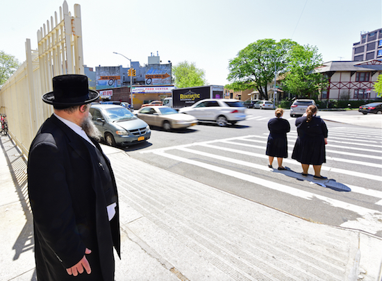 Rabbi Berel Hecht at one of his neighborhood’s dangerous intersections. He supports a bid for more speed cameras near schools, though his state Senator, Simcha Felder, does not. Eagle photo by Andrew Katz