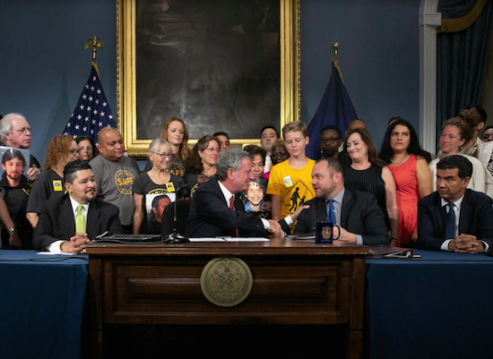 Surrounded by school children and public safety advocates, Mayor Bill de Blasio signed the speed camera bill into law. At right is City Council Speaker Corey Johnson. Photo from nycmayorsoffice/f