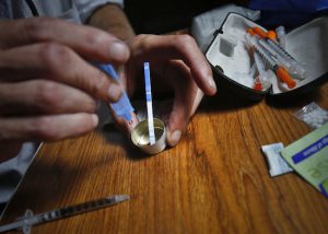 An addict prepares heroin, placing a fentanyl test strip into the mixing container to check for contamination, Wednesday Aug. 22, 2018, in New York. If the strip registers a "pinkish" to red marker then the heroin is positive for contaminants. AP Photo/Bebeto Matthews