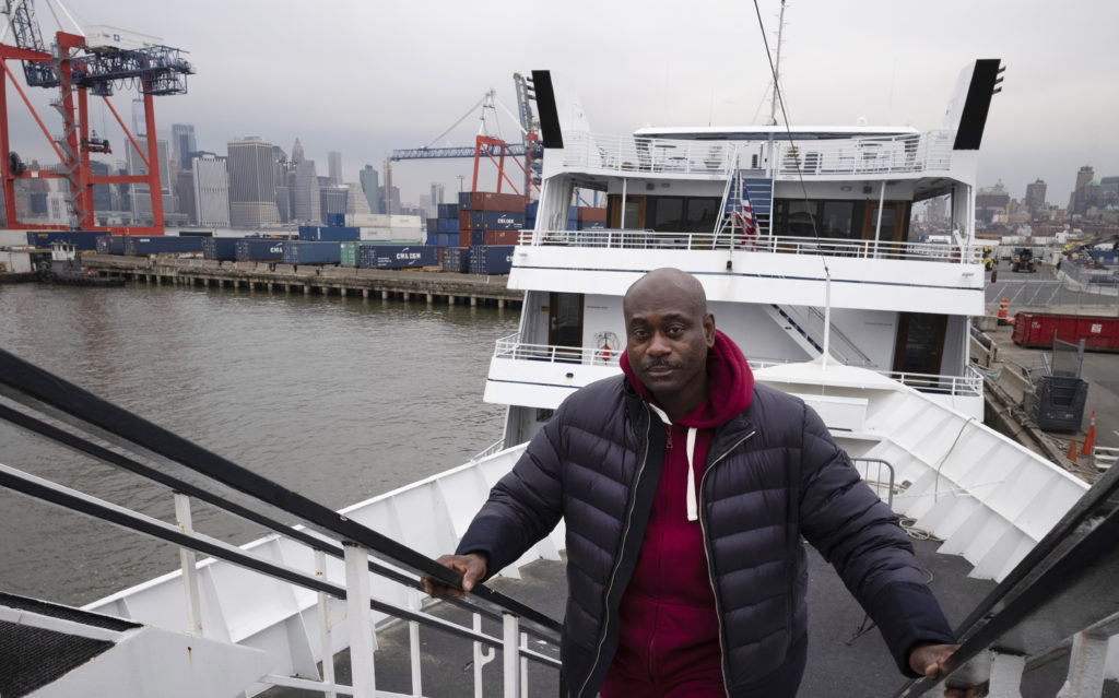 In this Nov. 30, 2018 photo, cruise boat owner Dwayne Braithwaite poses on his boat at a Brooklyn dock in New York. The boat owner is suing New York City, alleging that racism and corruption led to his ouster from city-owned docks. The city agency that runs the Brooklyn Army Terminal and Atlantic Basin docks says that’s not true and that the docking privileges for Braithwaite’s vessels were revoked because they were involved in multiple rules violations. (AP Photo/Mark Lennihan)
