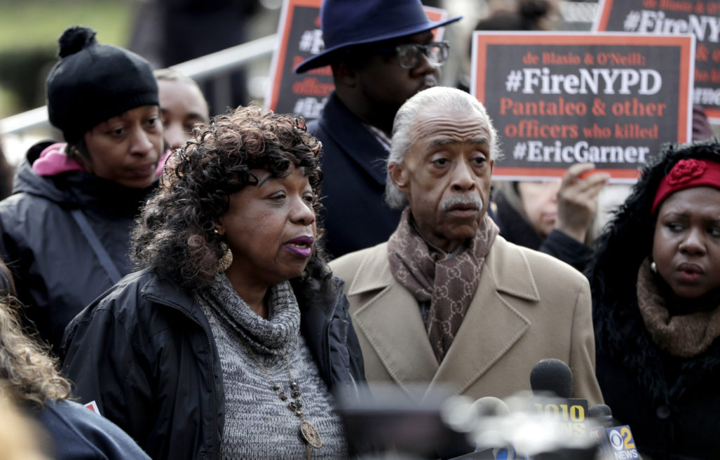 Gwen Carr, center, mother of Eric Garner, who was allegedly killed by a police chokehold maneuver, stands with Rev. Al Sharpton, right, during a news conference outside of New York Police headquarters, Thursday, Dec. 6, 2018, in New York. An administrative judge set a trial date for Daniel Pantaleo, the New York City police officer accused in the 2014 chokehold death of Garner. Pantaleo has been on desk duty since Garner's death on Staten Island. (AP Photo/Julio Cortez)