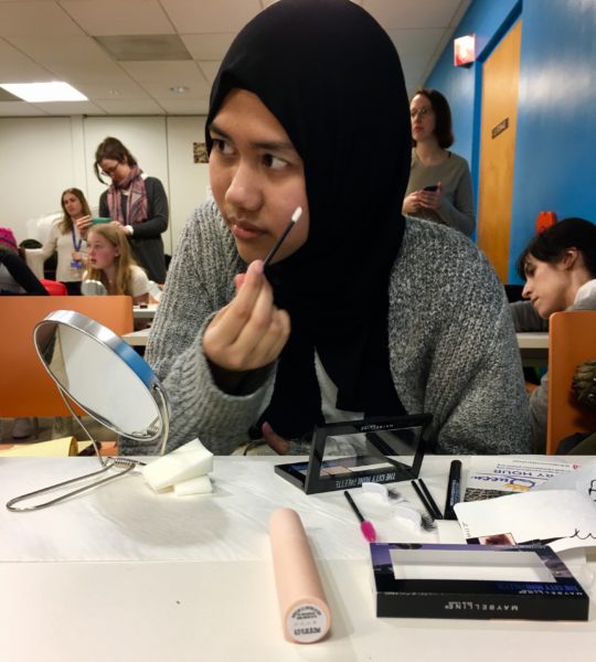 Teen girl in headscarf puts on makeup.