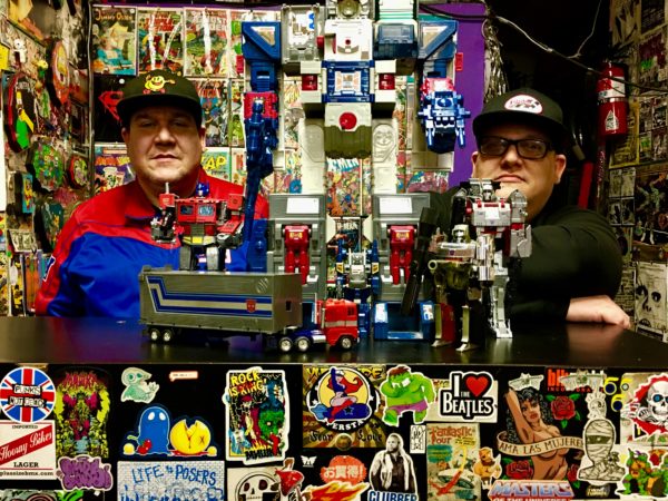 Pat Dellaratta at left and his brother, who uses the name Bizzid, pose with collectible Transformers at Dellaratta’s shop, Second Time Around. Eagle photo by Lore Croghan