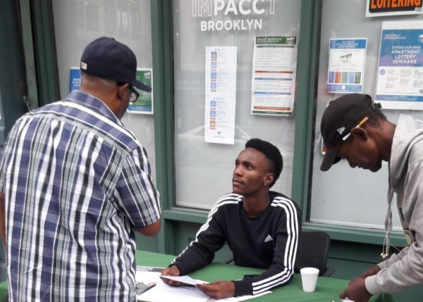 Raliek Gholson of IMPACCT Brooklyn, who’s seated at the table, interacts with community members outside one of the organization’s offices. Photo courtesy of IMPACCT Brooklyn 