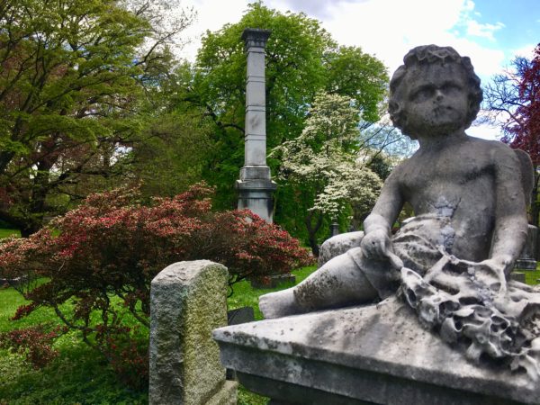 A cherub sits serenely among flowering trees in Green-Wood Cemetery. Eagle photo by Lore Croghan