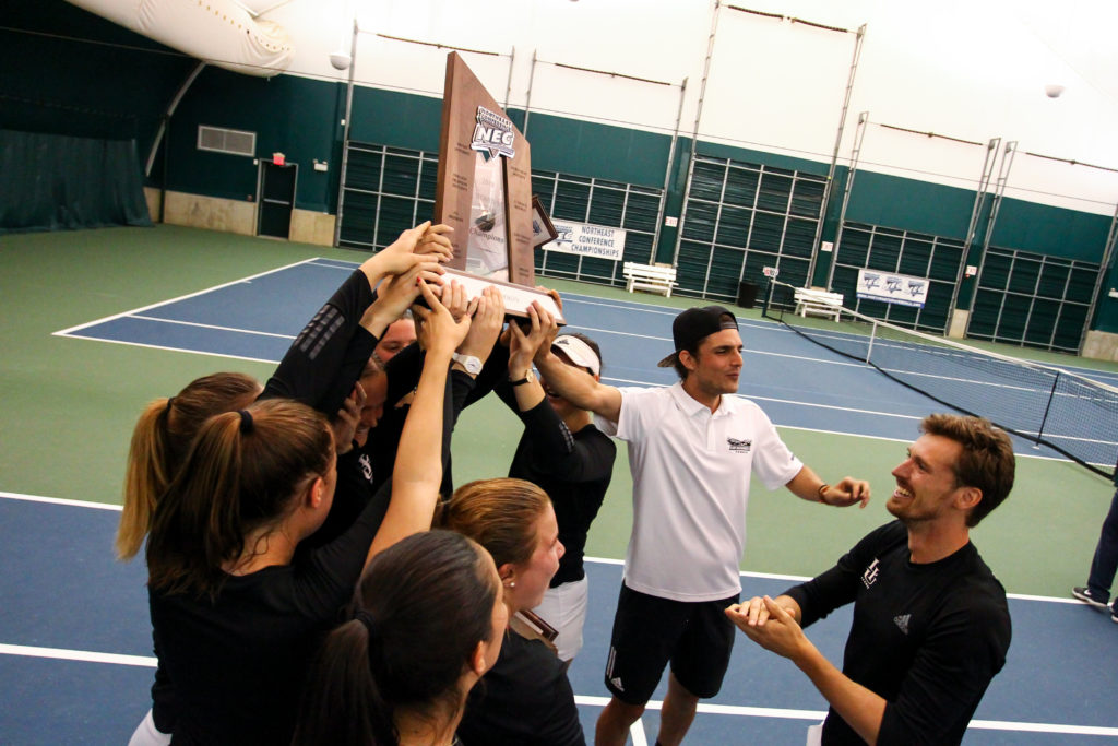 First-year LIU-Brooklyn head women’s tennis coach Jan Griga (far right) celebrates with assistant coach Pavlos Stephanides and his players after the Blackbirds clinched their record third consecutive Northeast Conference Championship in West Windsor, N.J., last Saturday. Photo Courtesy of LIU-Brooklyn Athletics