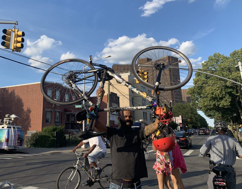 A cyclist raises his bike in the air after a moment of silence for Ernest Askew, who was struck and killed in Brownsville last week. Eagle photo by Noah Goldberg