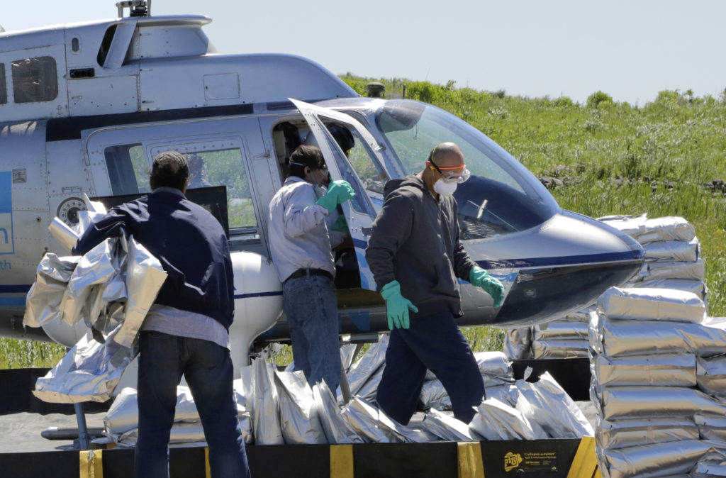 Workers with the New York City Health Department load bags of mosquito larvicide into pods on the side of a helicopter for aerial treatments in 2016. AP photo by Mark Lennihan