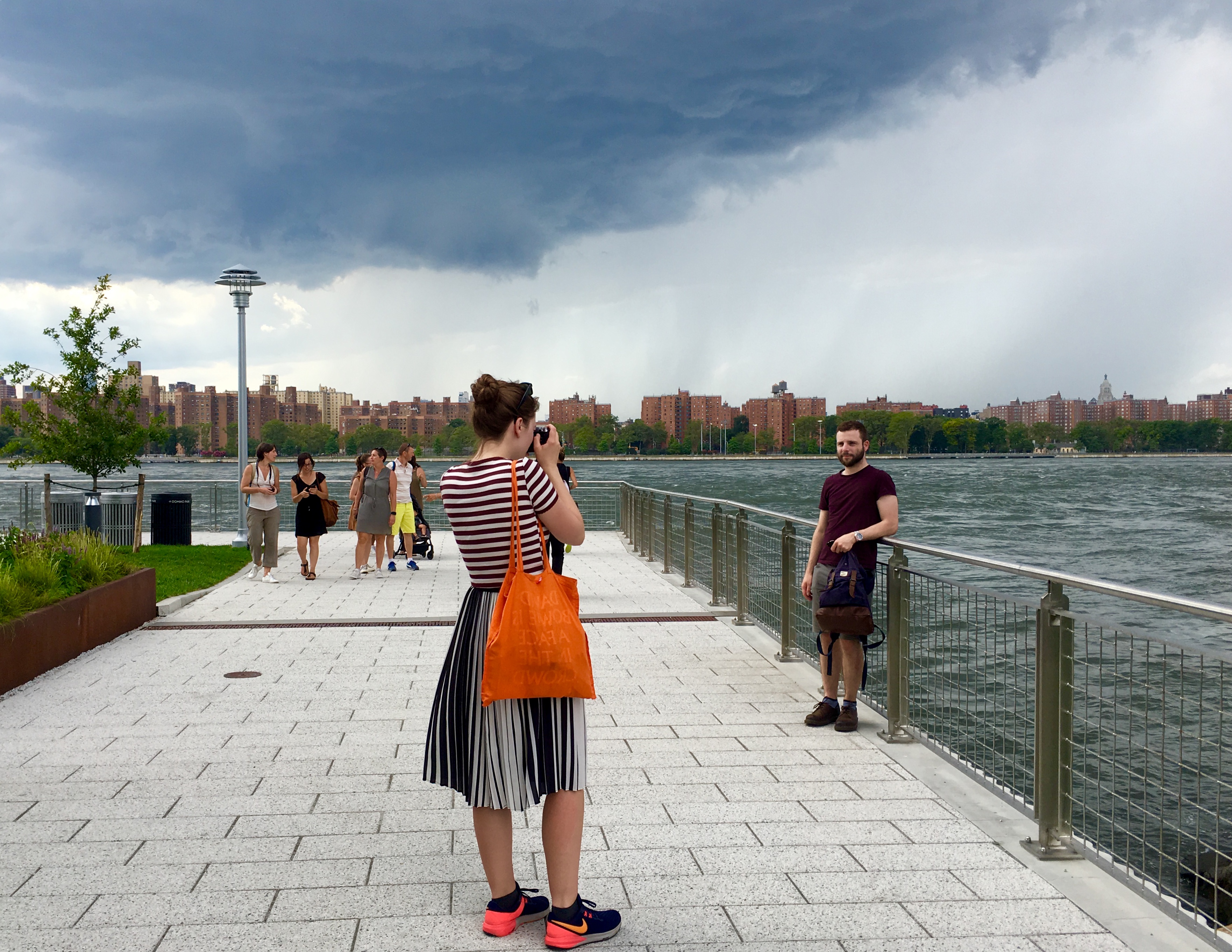 People pose for pictures on Domino Park’s esplanade while a dark cloud looms. Eagle photo by Lore Croghan