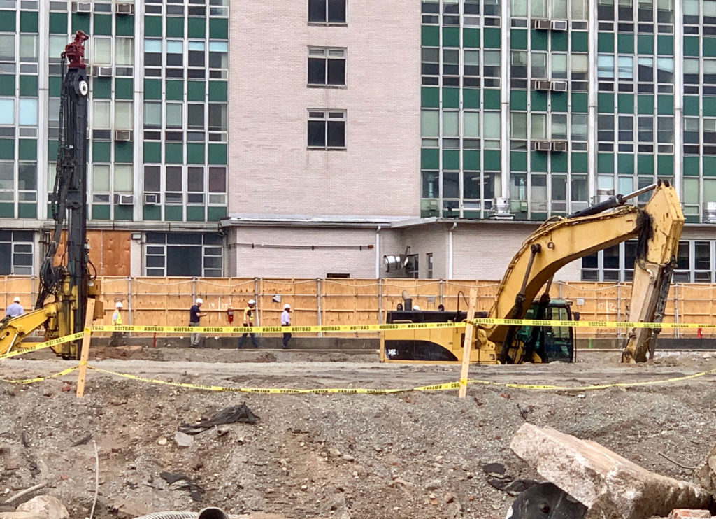 City inspectors and other personnel walk past the pit at 196 Willoughby St. on LIU’s Brooklyn campus where excavation equipment hit a live electric line and caused an explosion. Eagle photo by Mary Frost