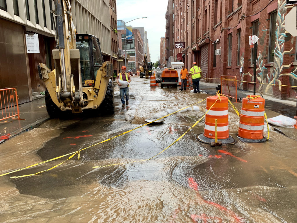 A water main break flooded Water Street in DUMBO for hours on Thursday, backing up sewage into the surrounding basements. Shown: Workers for Halcyon Construction Corp. placed sandbags on Water Street to funnel the water into the sewer. Eagle photo by Mary Frost