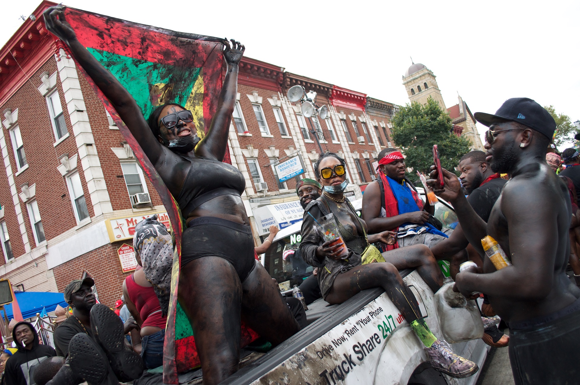 A woman dances in the back of a truck while holding the flag of Grenada on Nostrand Avenue.